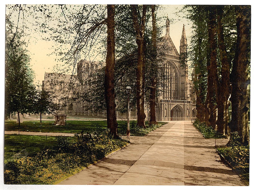 Winchester Cathedral seen along a tree-lined avenue, in an old color print.