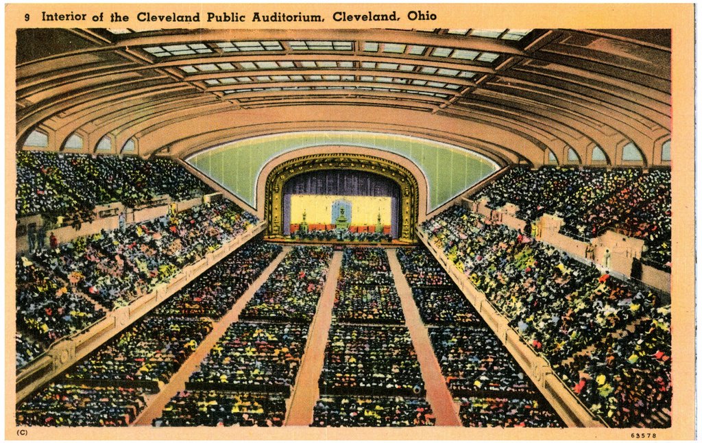 A color postcard of the interior of Cleveland’s Public Auditorium: a vast hall with a stage and tiers of seats.