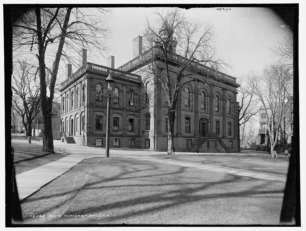 A stone school building with a cupola, set in a park.