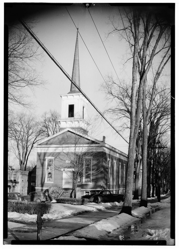 A white church with a tall steeple in a village.