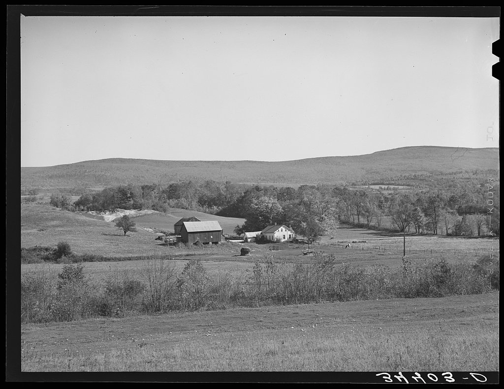 A Vermont farm in a valley below wooded hills.