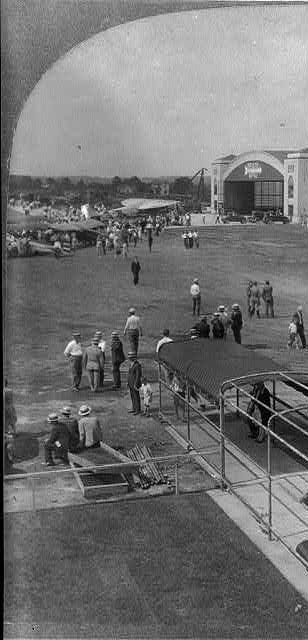 Spectators at a flying field watching a biplane.