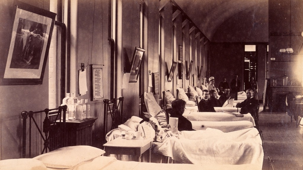 A long men’s ward at Bellevue Hospital, with rows of beds and patients’ case notes clipped to the wall above them.